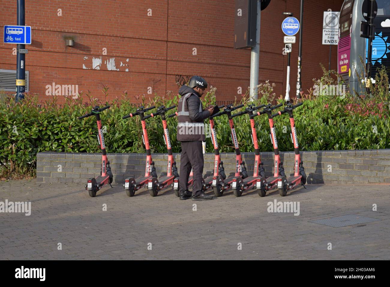 A member of staff at Voi Scooters checks a row of electric hire scooters outside the Bull Ring, Grand Central, Birmingham. August 2021 Stock Photo