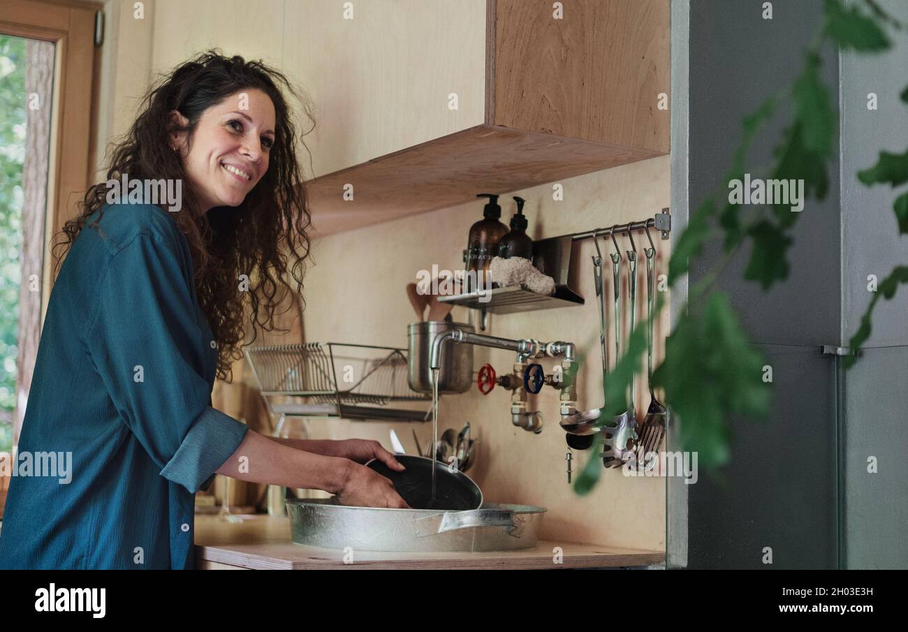 Happy young woman washing up indoors in a tree house. Stock Photo