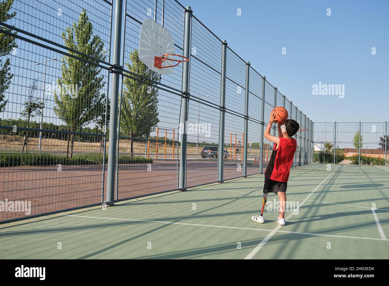 Basketball kid player with a leg prosthesis throwing the ball to the basket. Stock Photo