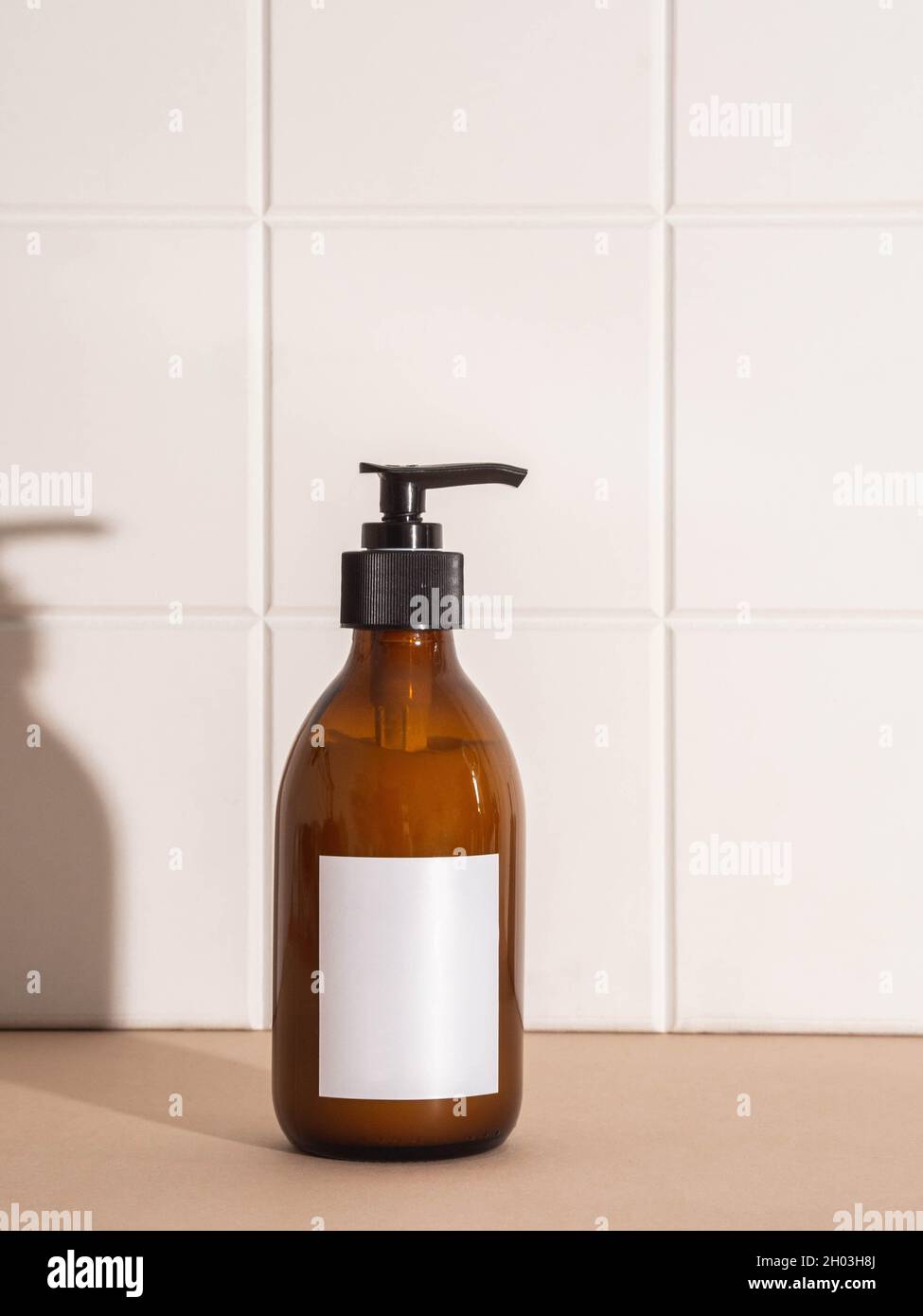 Amber bottle with white label mockup for bathing products in bathroom, spa shampoo, shower gel, liquid soap on beige table and white wall tile front v Stock Photo
