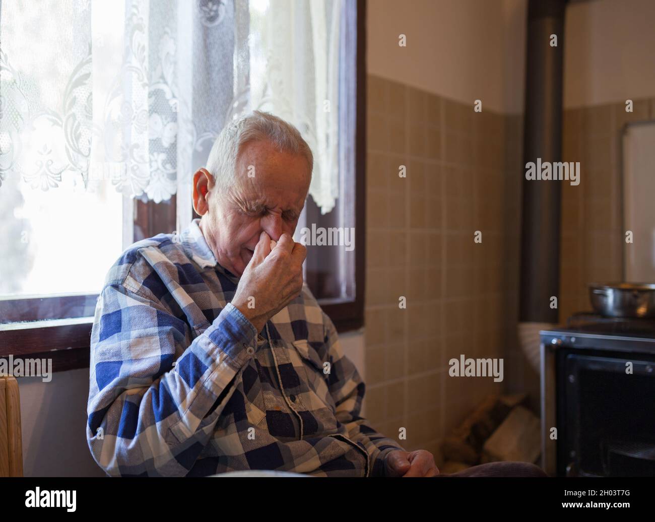 Old man holding tissue while sneezing at home. Virus and grippe concept Stock Photo