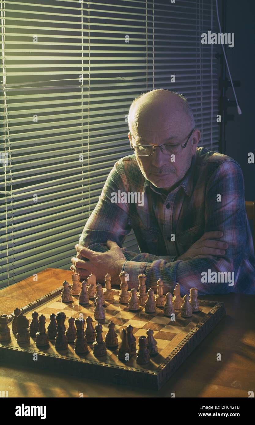 Old man sitting at table beside window with blinds and playing chess Stock  Photo - Alamy