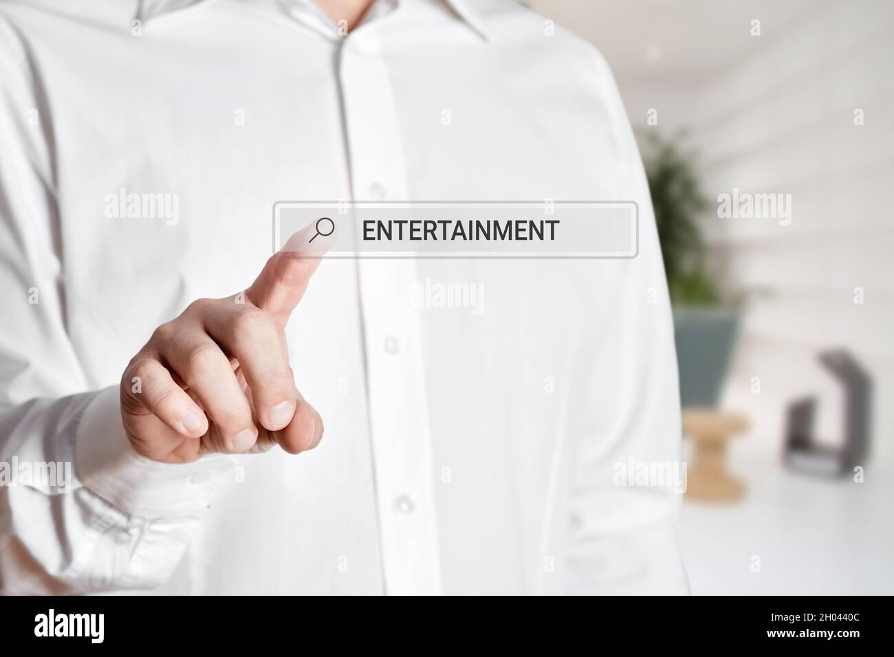 Man press the search bar icon on a virtual screen with the word entertainment. Online search for entertainment on the internet Stock Photo