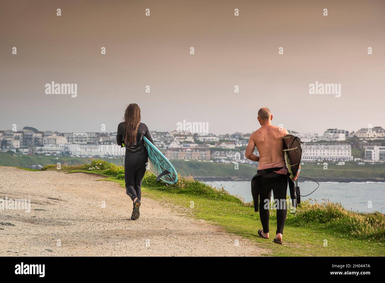 Male and female surfers carrying their surfboards and walking on the coast path to Fistral in Newquay in Cornwall. Stock Photo