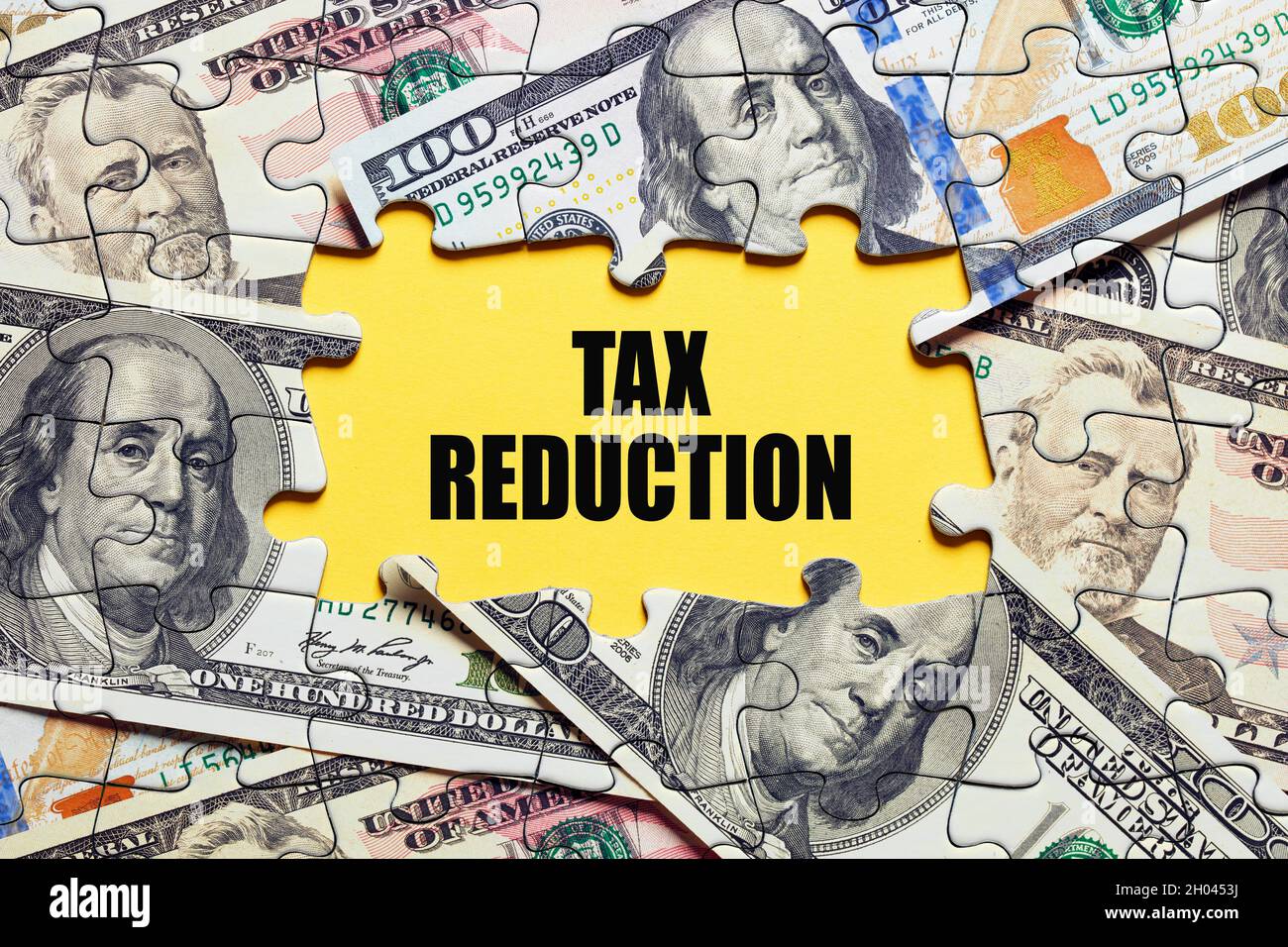 The word tax reduction surrounded by puzzle pieces with dollar bill money. Cut, refund or deduction in taxation concept.. Stock Photo