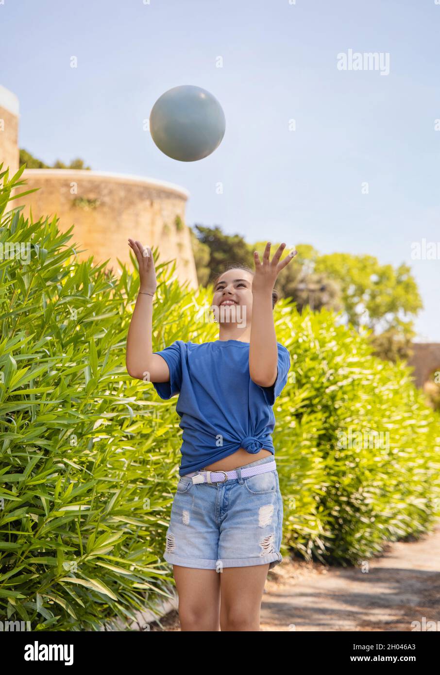 Happy schooler girl in blue t-shirt holding ball outdoors. Cute child doing sports, enjoying playing soccer and having fun in park. Active hobbies, he Stock Photo