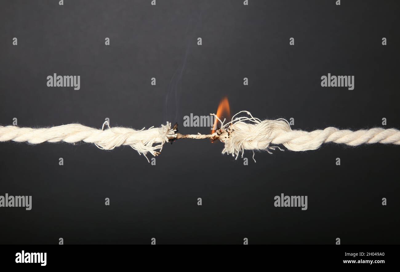 Burning frayed rope at breaking point on gray background Stock Photo