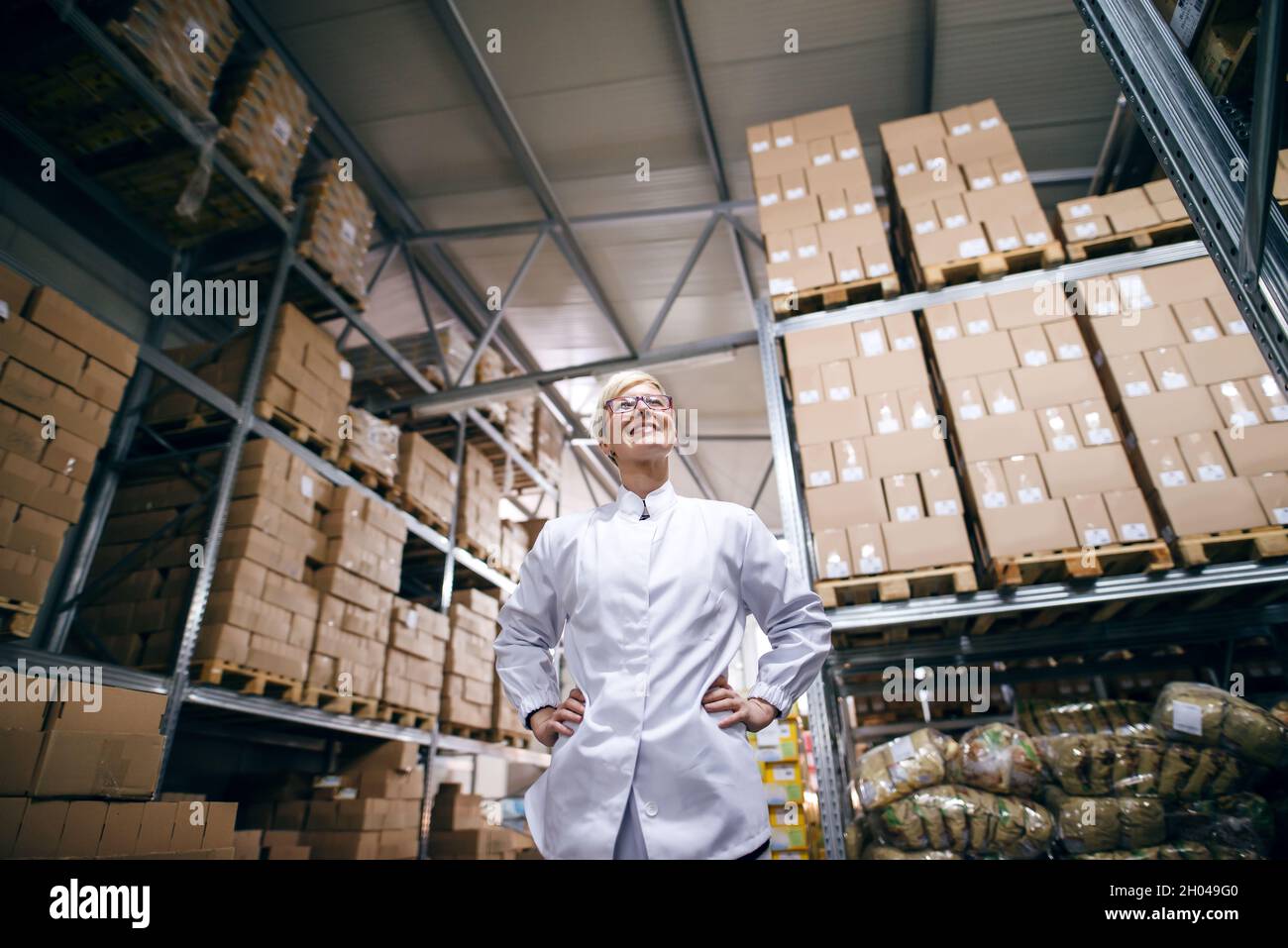 Bottom view of female factory worker standing with hands on hips. Warehouse interior. Stock Photo