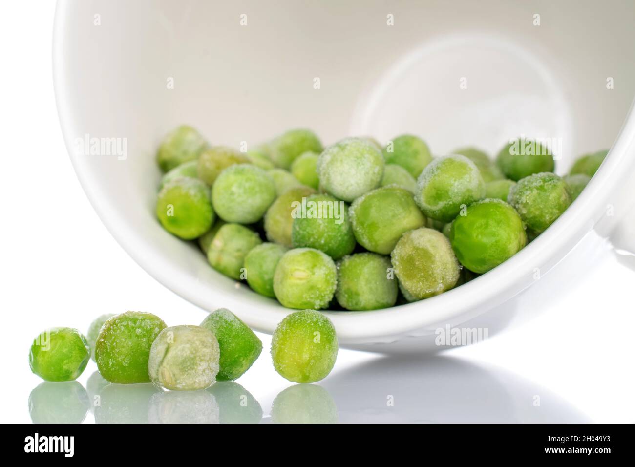 Organic frozen green peas in a white ceramic cup, closeup, isolated on