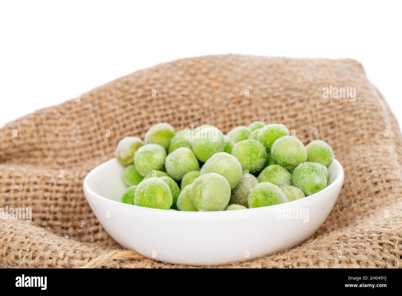 Organic frozen green peas in a white saucer on a jute fabric, closeup