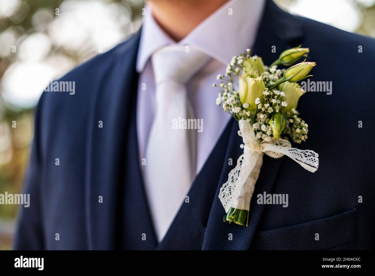 Unrecognizable young groom in elegant dark blue suit with beautiful white roses boutonniere. Groom fashion detail shot. Stock Photo