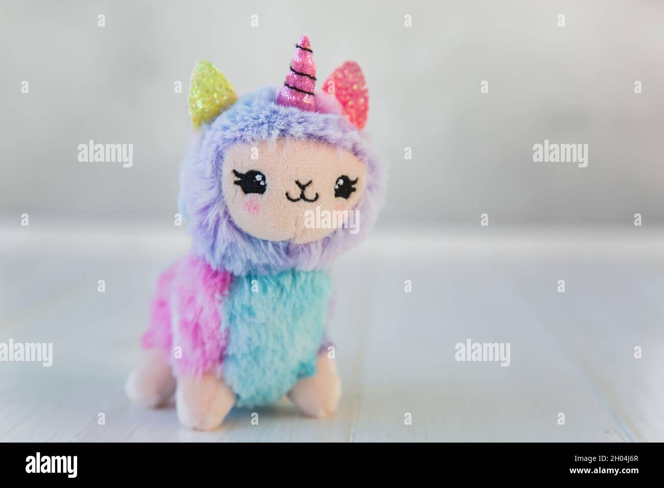 Colored plush llama unicorn on white wooden background. Famous and