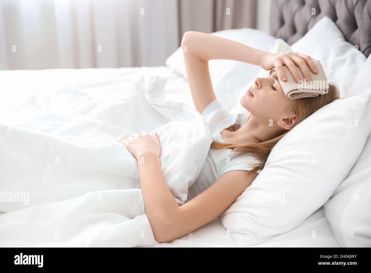 Teenage girl suffering from headache while lying in bed at home Stock