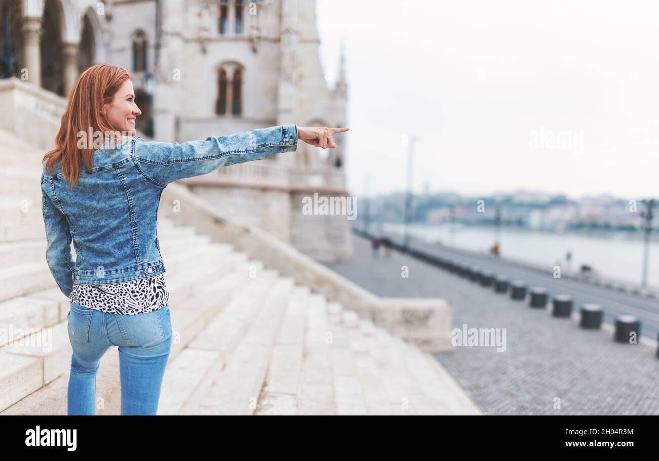 Redhead hungarian urban woman pointing into distance at Parliament building, Budapest, Hungary, widescreen Stock Photo