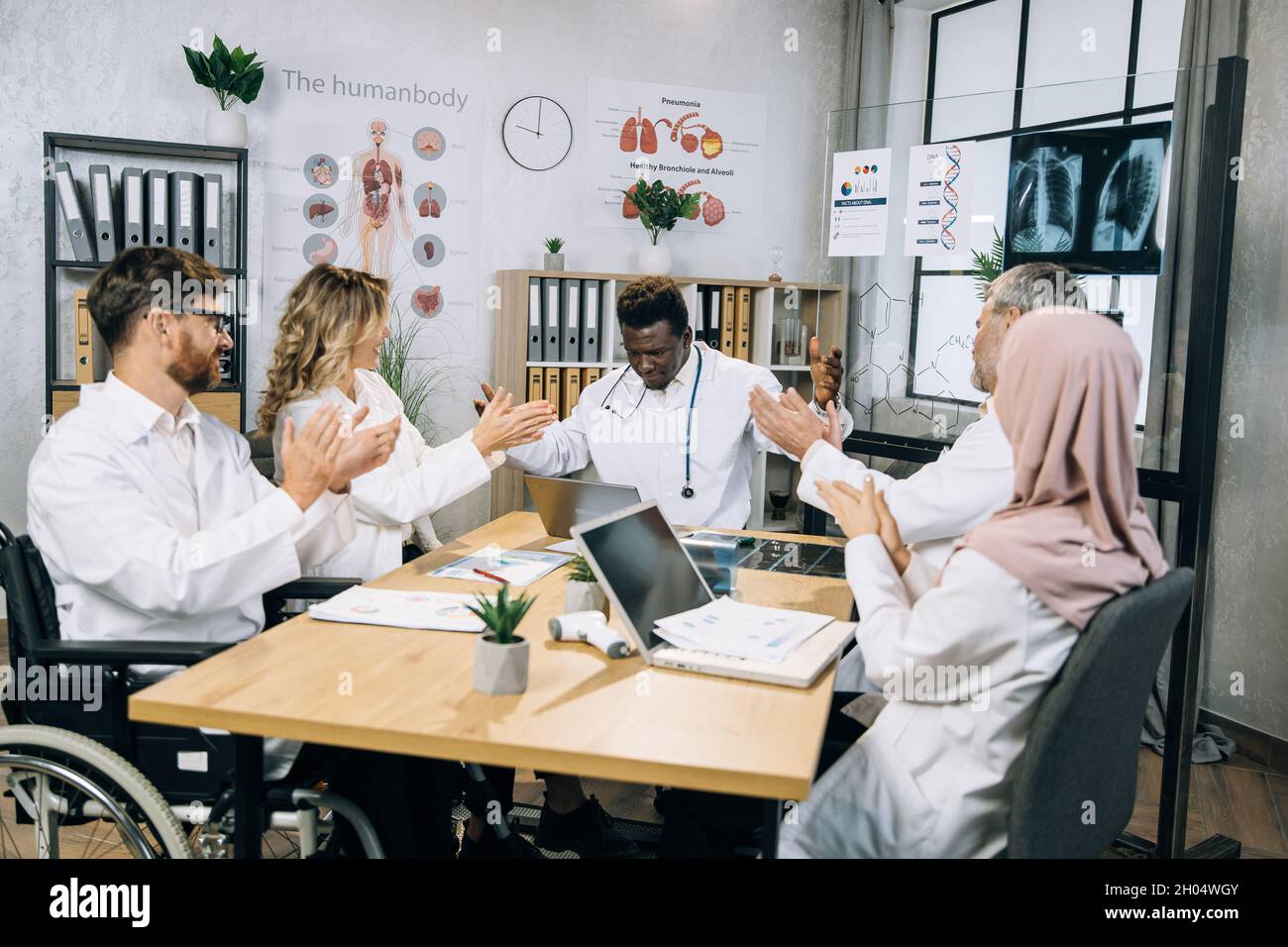 Group of multiracial therapists in white lab coats applauding to african american doctor after