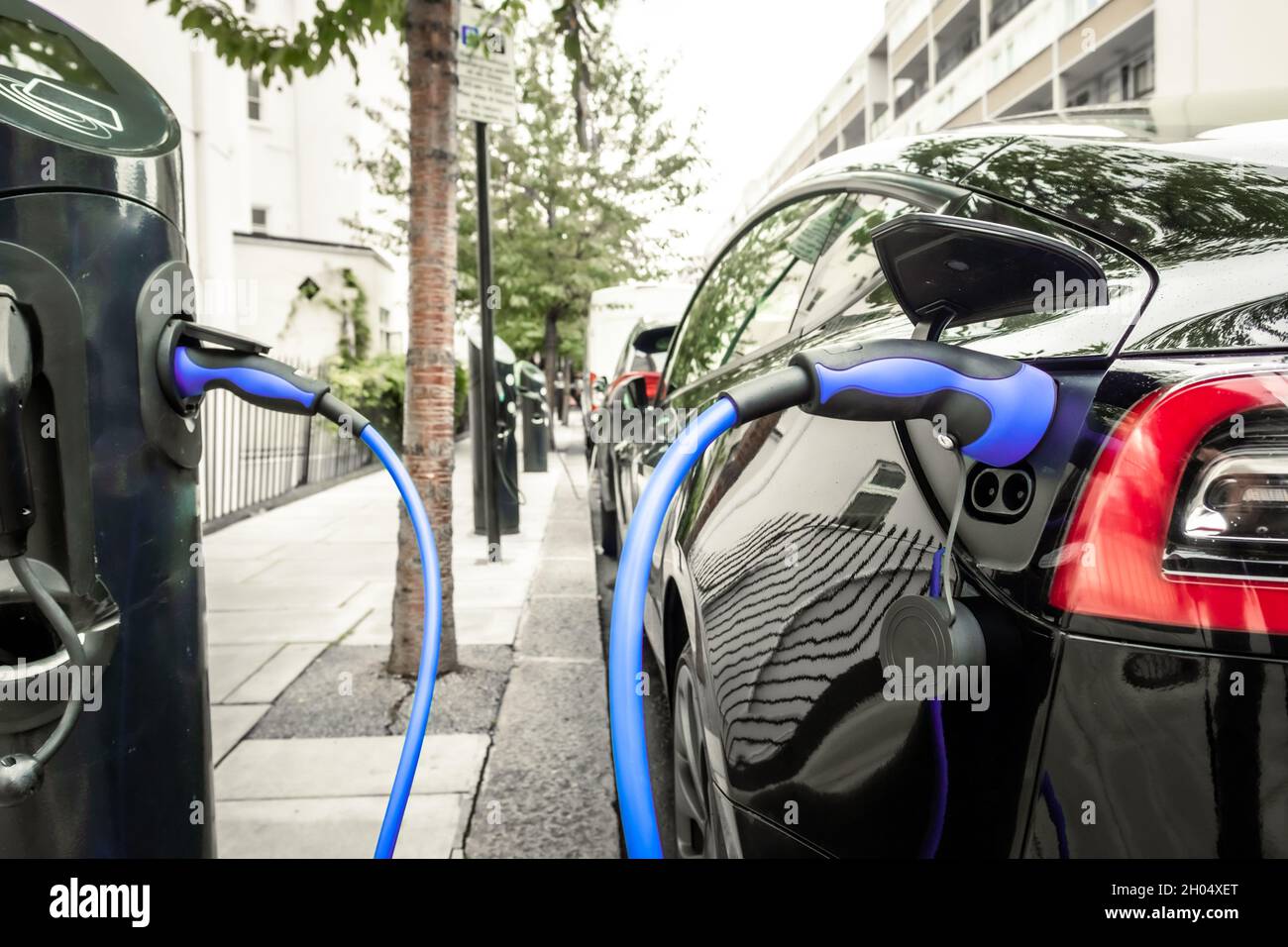 Electric car plugged in and changing on urban city street Stock Photo