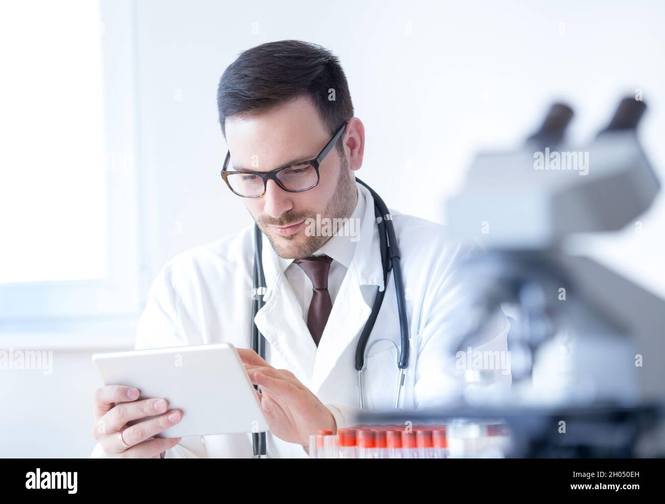 Young attractive doctor working on tablet in laboratory with blood samples and microscope Stock Photo