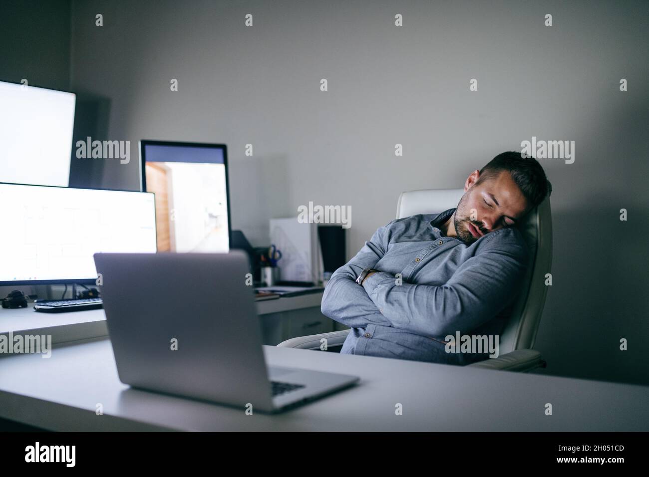 Young bearded Caucasian employee sleeping in the chair in office. Arms