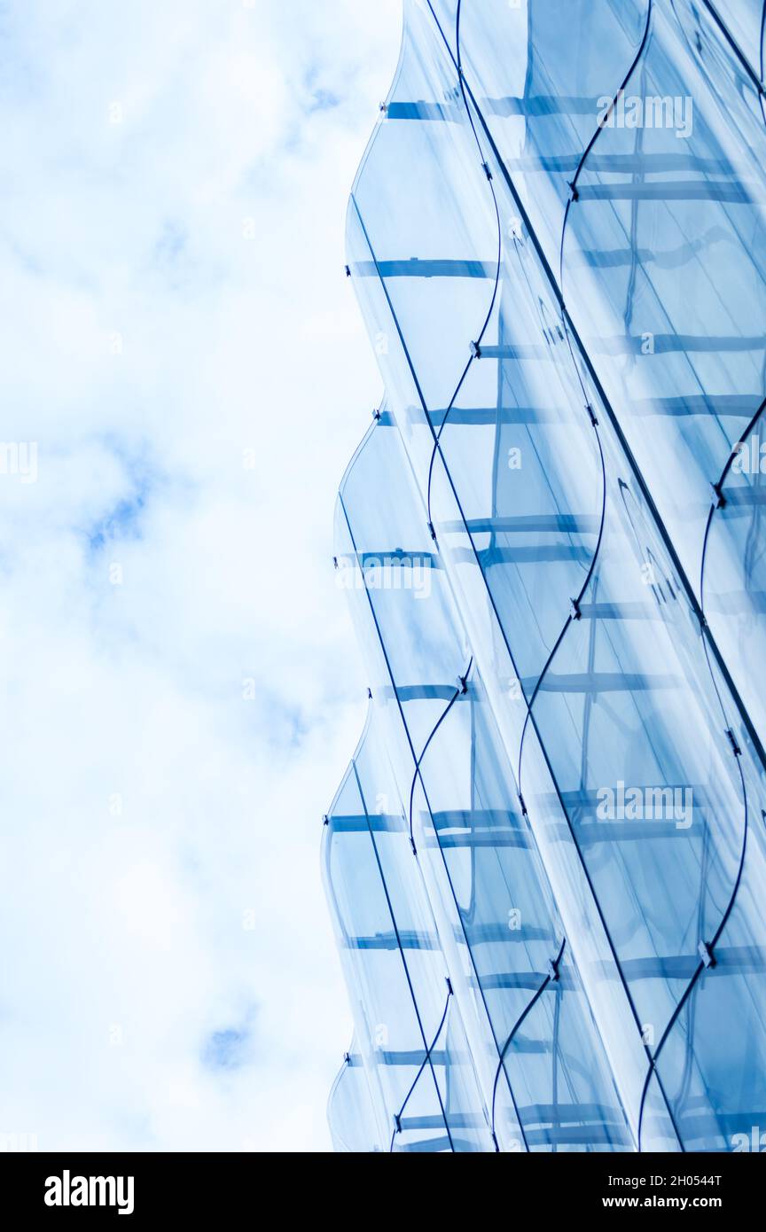 Detail of the wavy glass curtain wall facade of a nice modern building, sky and clouds reflecting on it Stock Photo