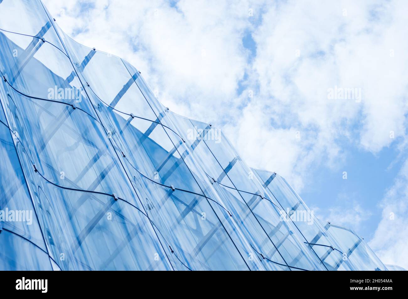 Detail of the wavy glass curtain wall facade of a nice modern building, sky and clouds reflecting on it Stock Photo