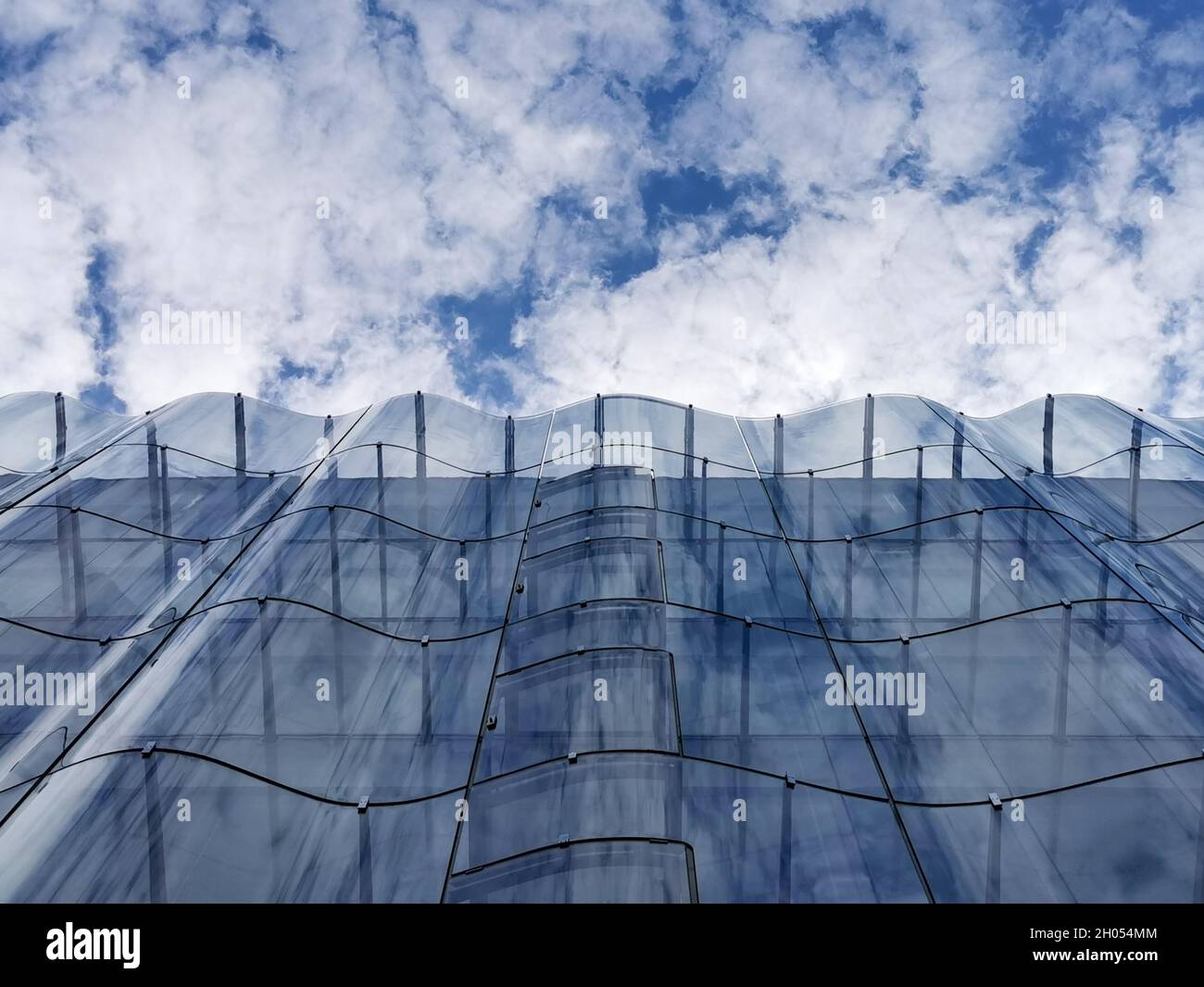 Detail of the wavy glass curtain wall facade of a nice modern building, sky  and clouds reflecting on it Stock Photo - Alamy