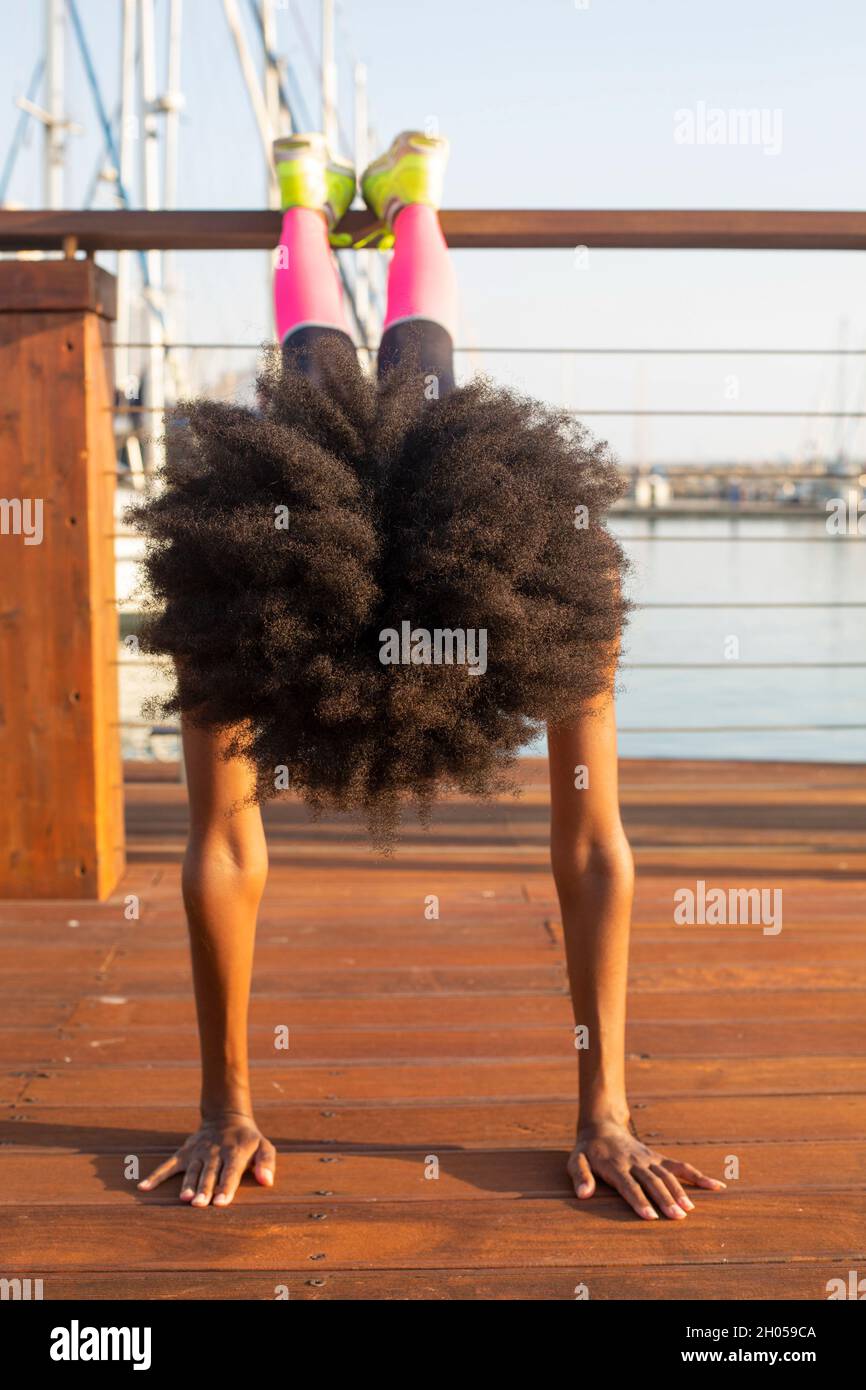 Young athletic woman in sports clothes stretching on a mat on a wooden deck in a marina Stock Photo