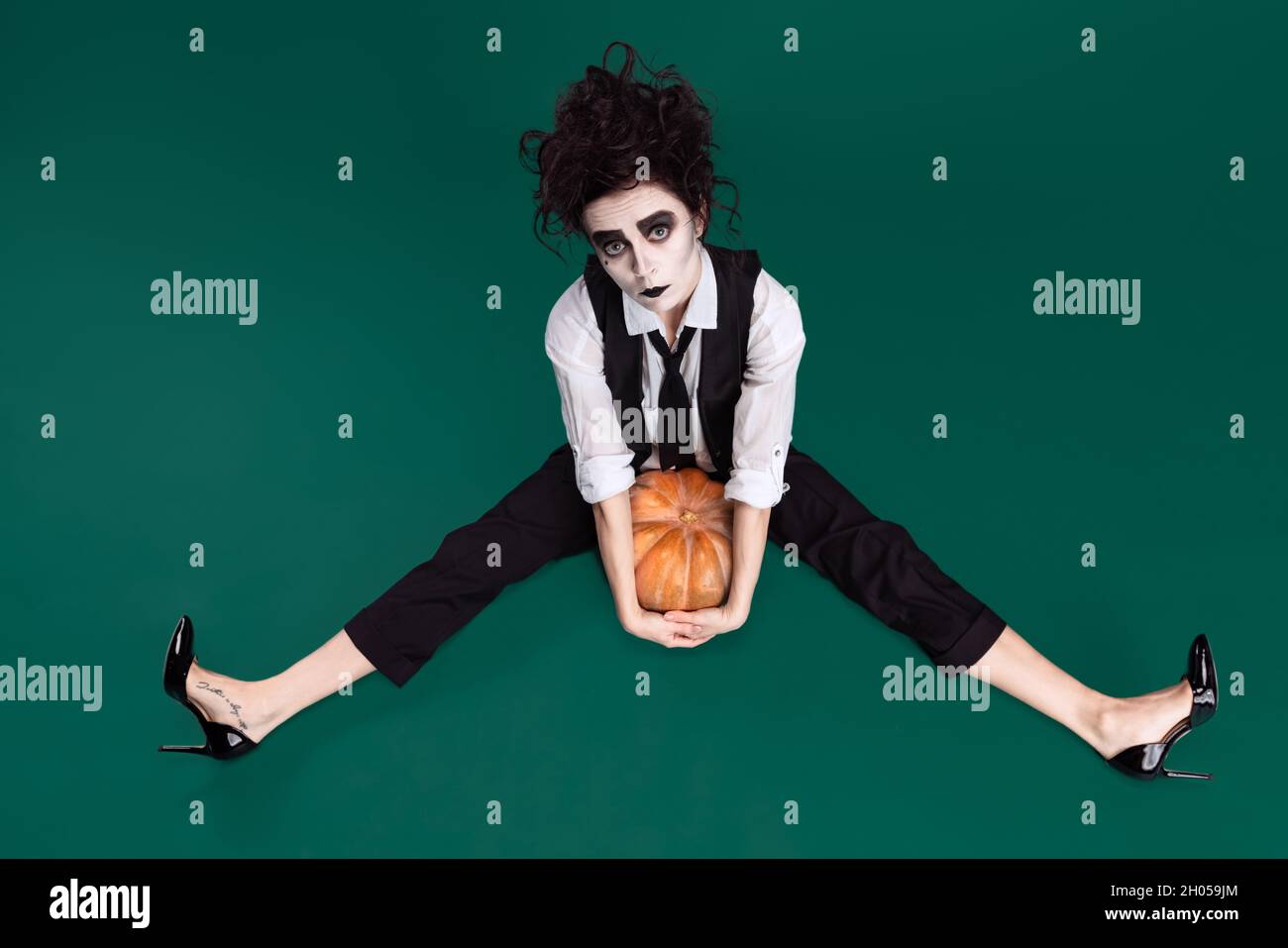 Top view portrait of expressive woman wearing costume of famous movie character, sitting with pumpkin isolated over green background Stock Photo