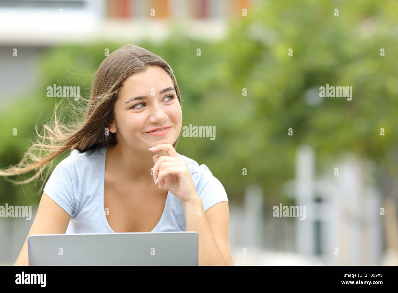 Happy teen with a laptop thinking looking at side in a park with copy space Stock Photo