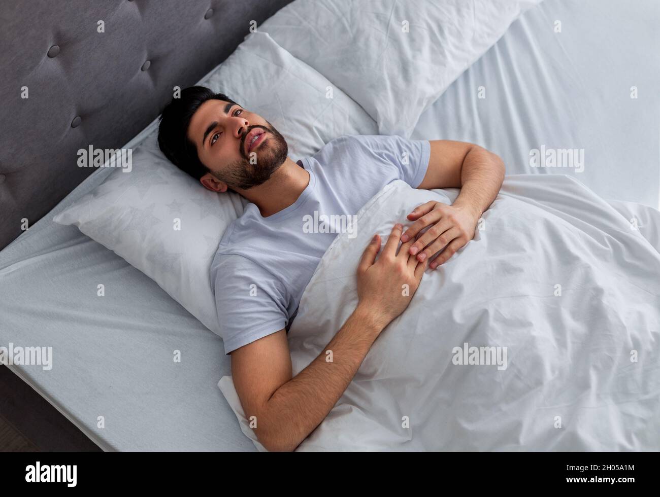 Thoughts in head not let fall asleep. Young arab man lying in bed and