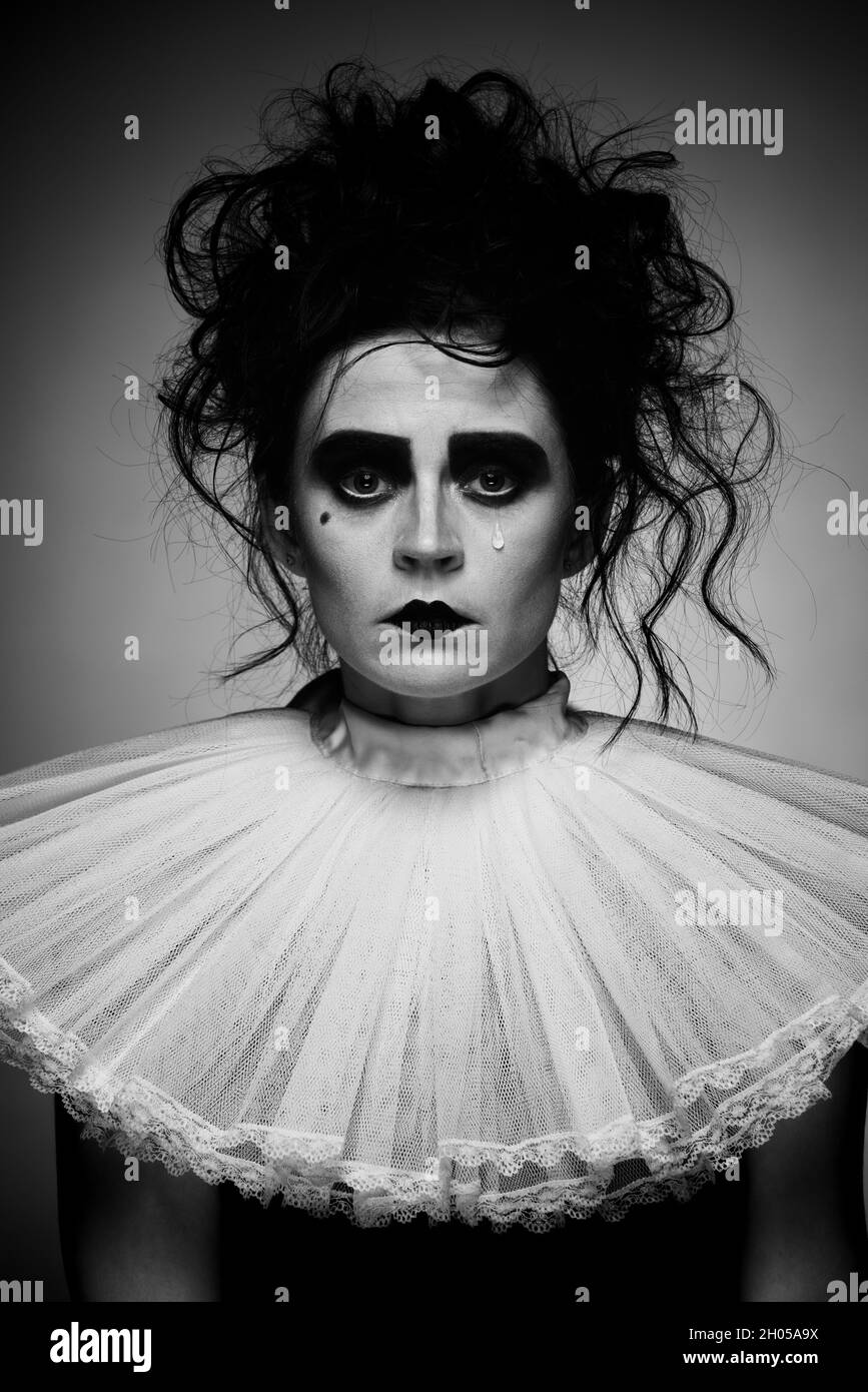 Portrait of creepy looking crying woman in vintage costume and spooky makeup isolated over dark background. Black and white image. Halloween Stock Photo