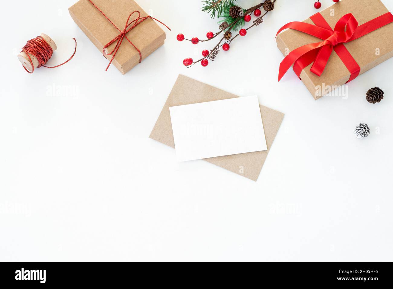 Christmas composition. Blank greeting card, envelope mockup.Decoration with christmas gifts with red bow, red berries, ribbon, fir tree branches and p Stock Photo
