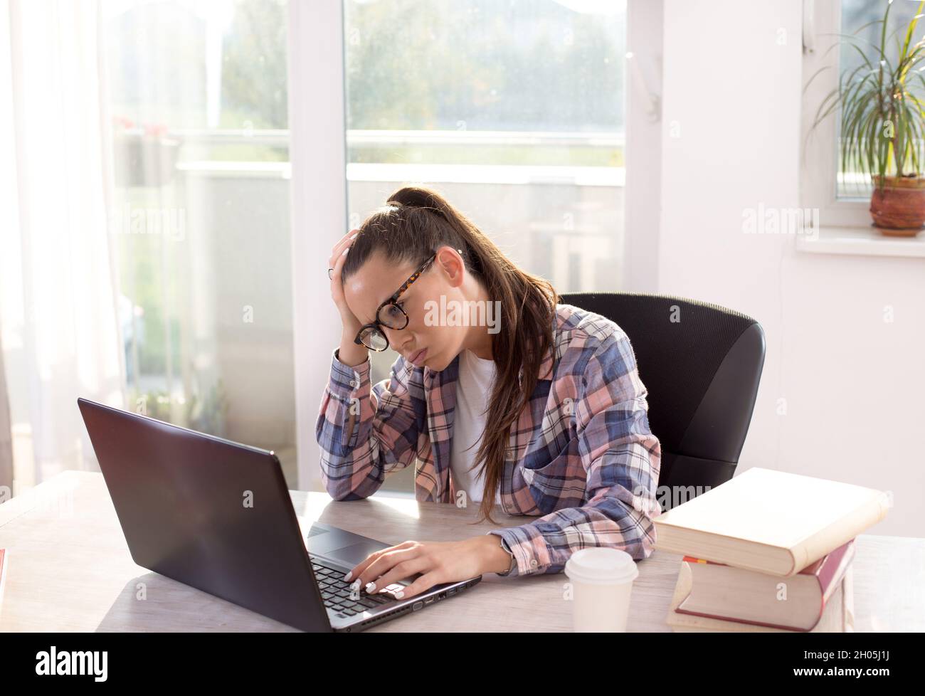 Pretty young woman studying in front of laptop and big books on table ...