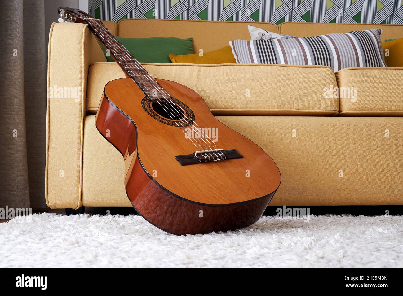 Classic guitar on the carpet close to the soft elegant yellow sofa. Musical instruments in interior and design Stock Photo