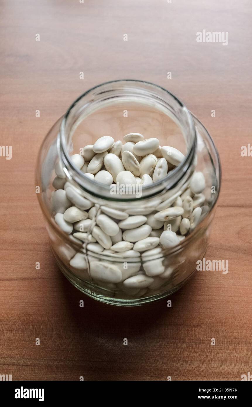 White beans (Phaseolus vulgaris) in a glass jar on wooden desk, flat lay view from directly above Stock Photo