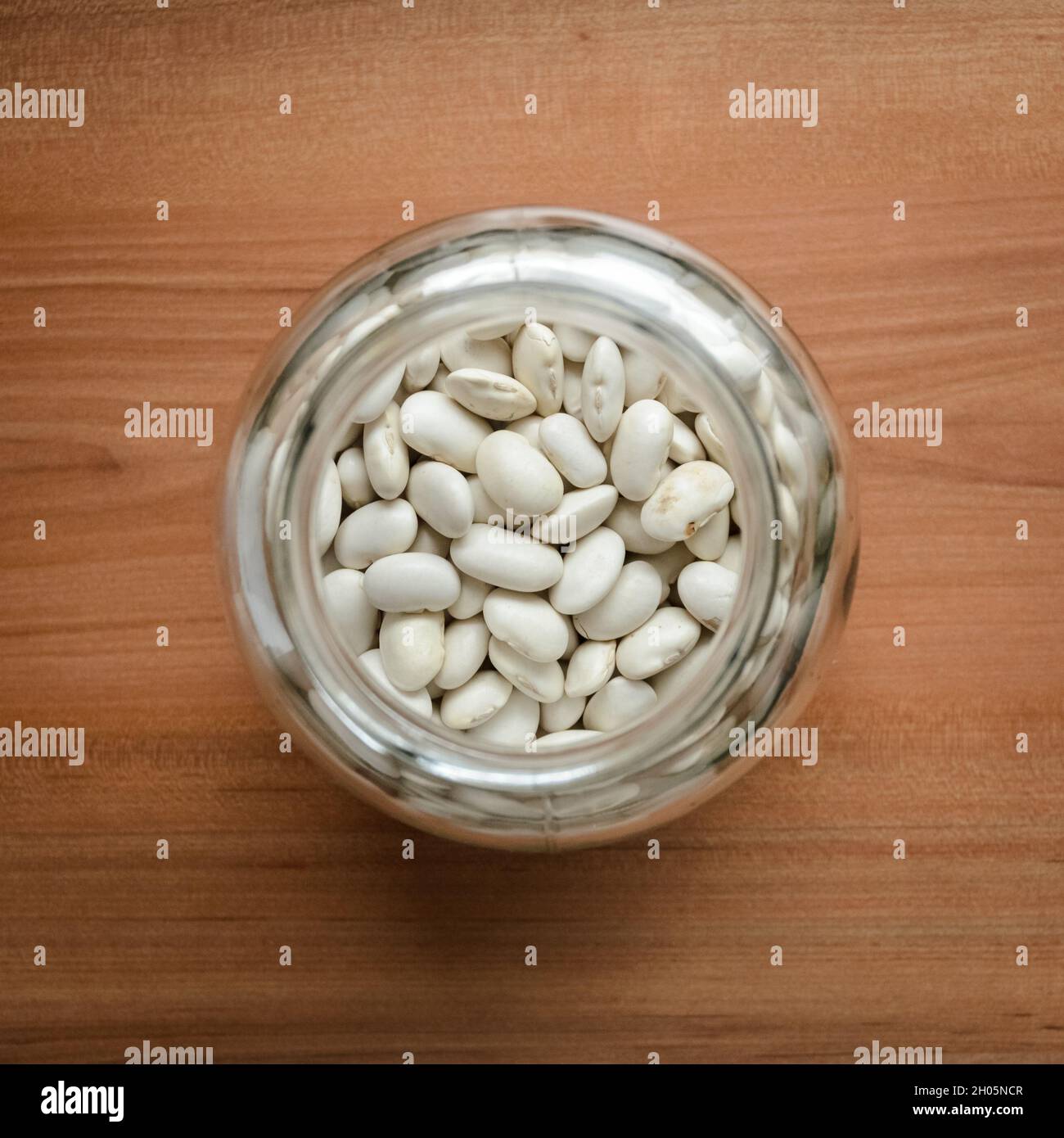 White beans (Phaseolus vulgaris) in a glass jar on wooden desk, flat lay view from directly above Stock Photo