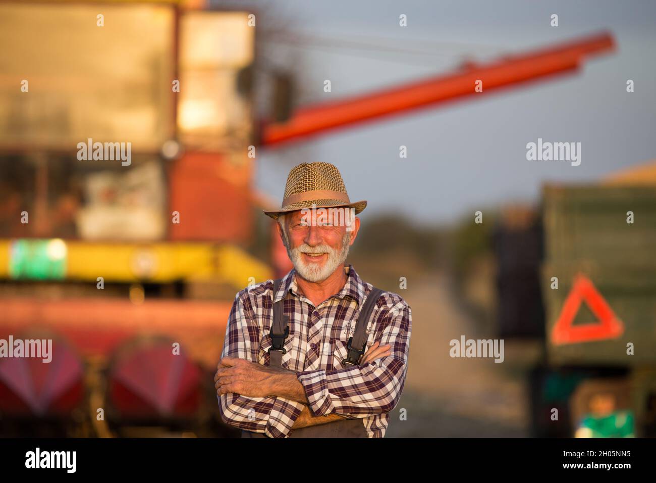 Portrait of senior farmer standing with crossed arms in front of ...