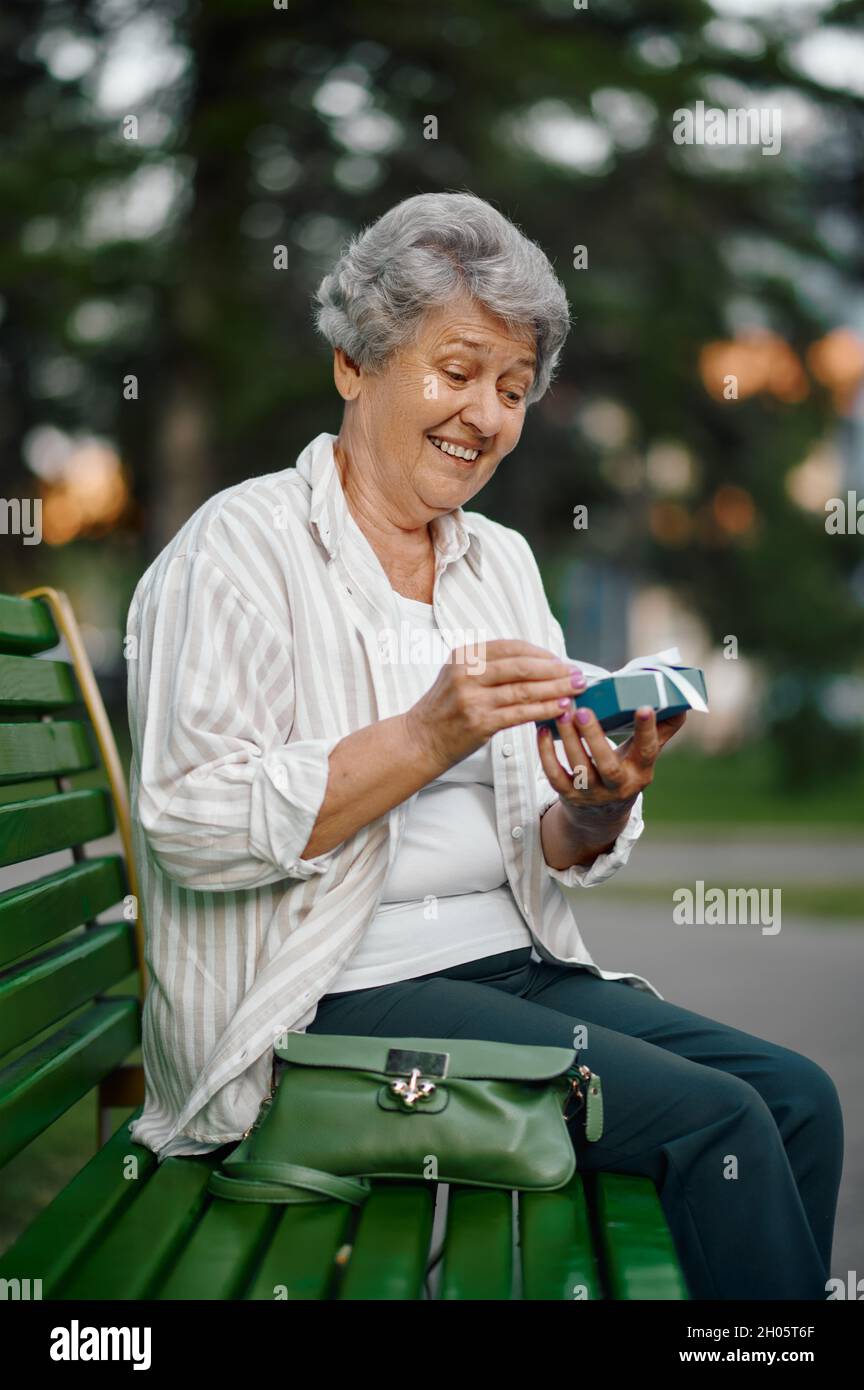 Granny Bench Cheerful granny opens a gift box on the bench Stock Photo - Alamy