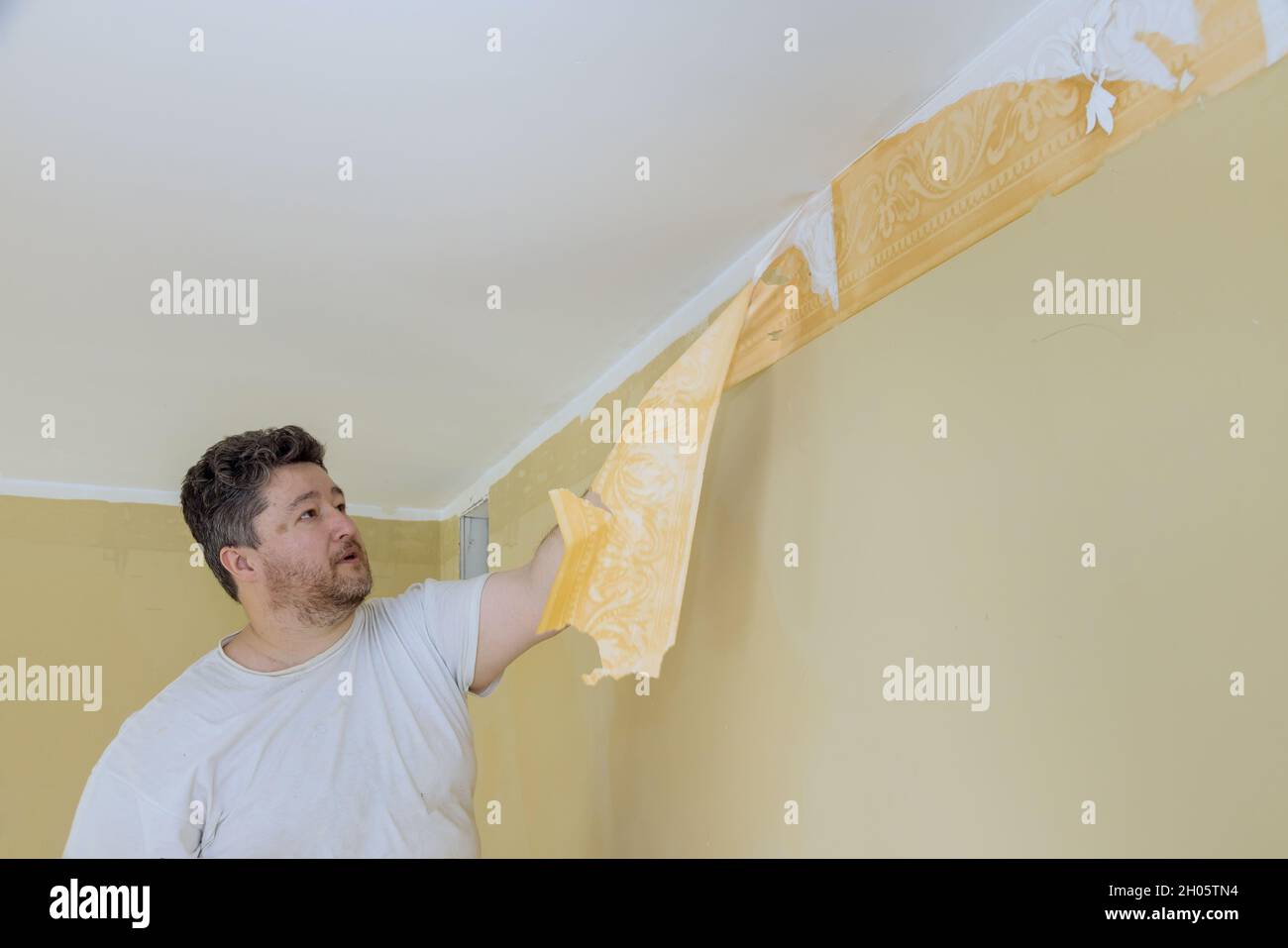 Manual work with scraper worker hand scraping old wallpaper on wall