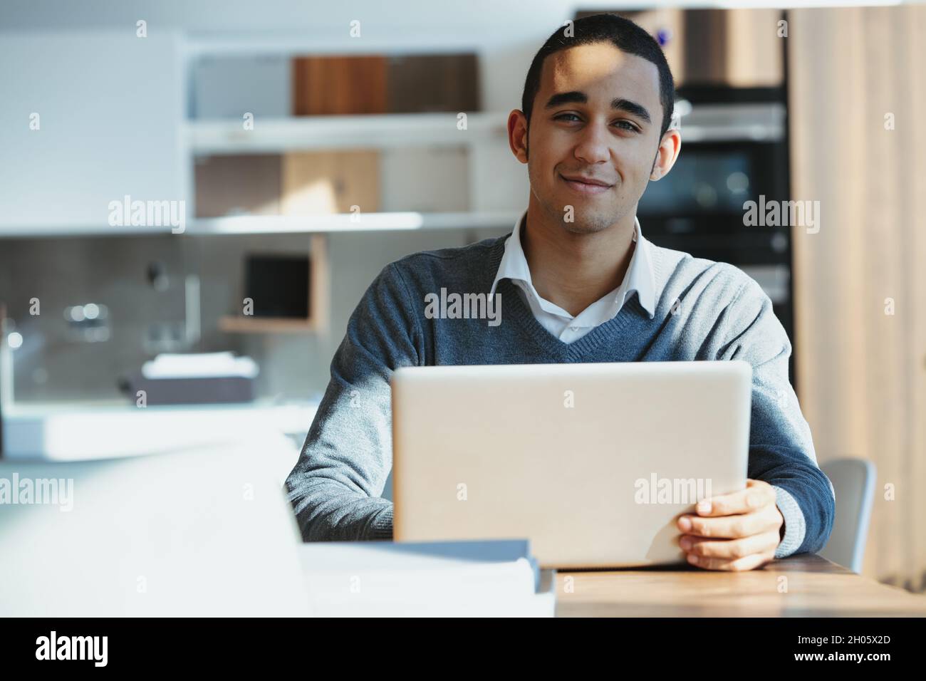 Young Black businessman seated at a laptop computer in sunshine in an office looking at the camera with a quiet smile Stock Photo