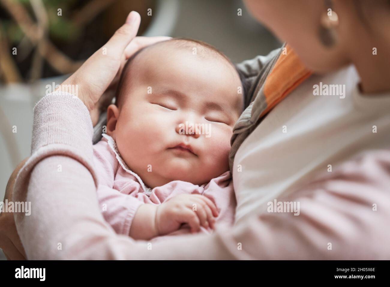 Close-up of mother holding her sleeping baby cradling her and stroking on the head Stock Photo