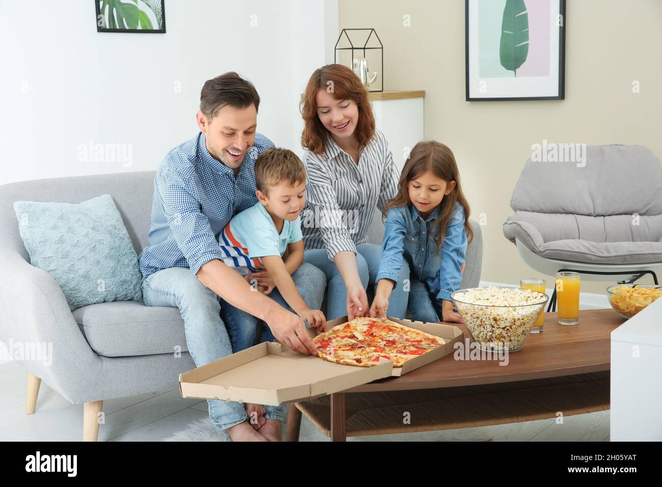 Family eating pizza while watching TV in room Stock Photo Alamy
