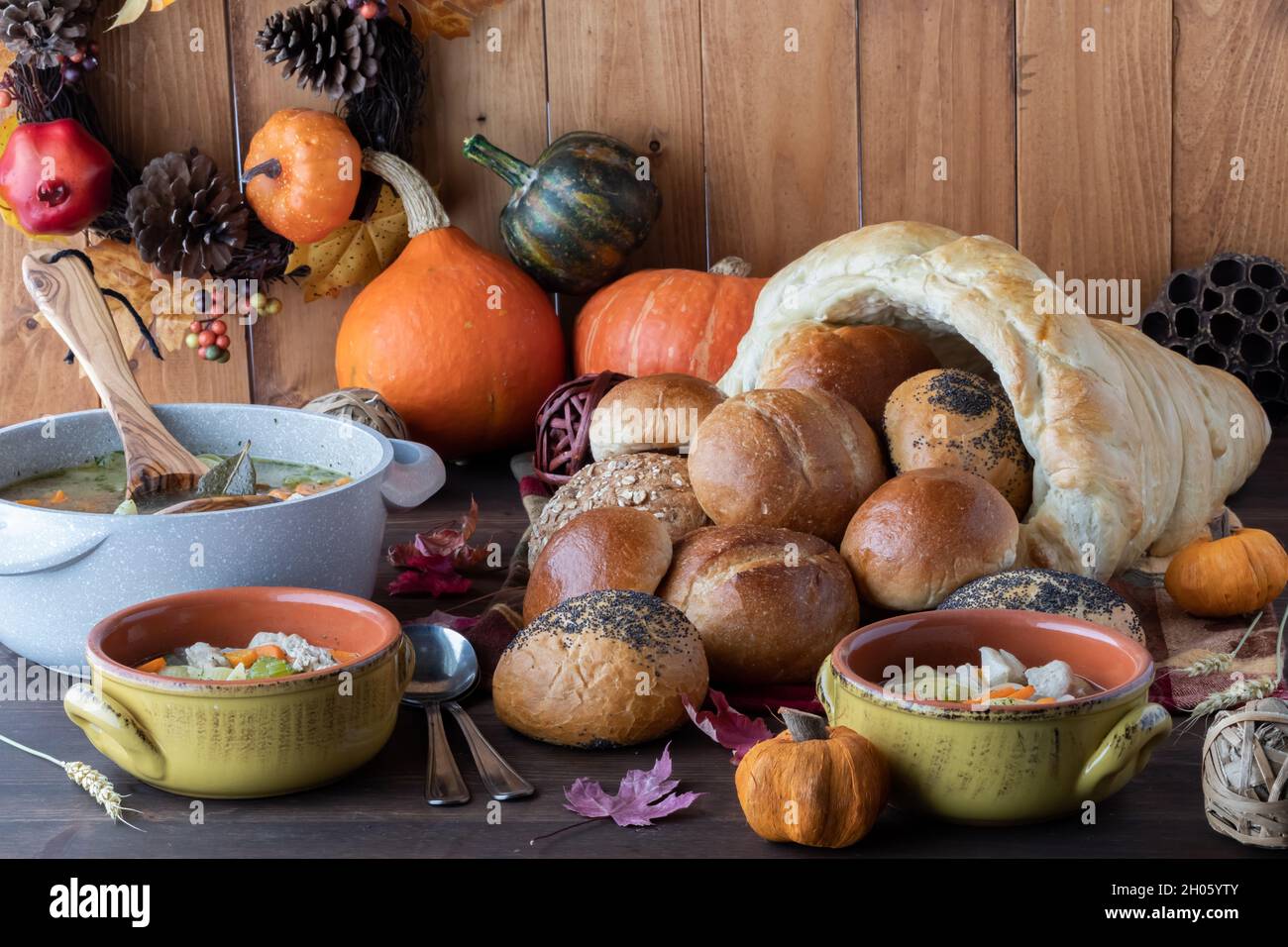 Bowls of turkey soup with Thanksgiving decorations and a cornucopia of buns. Stock Photo