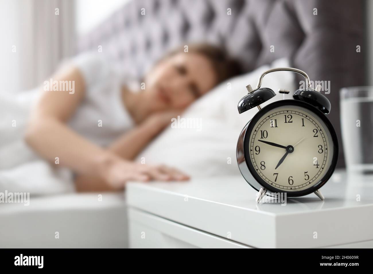 Alarm clock on nightstand of young woman suffering from headache Stock
