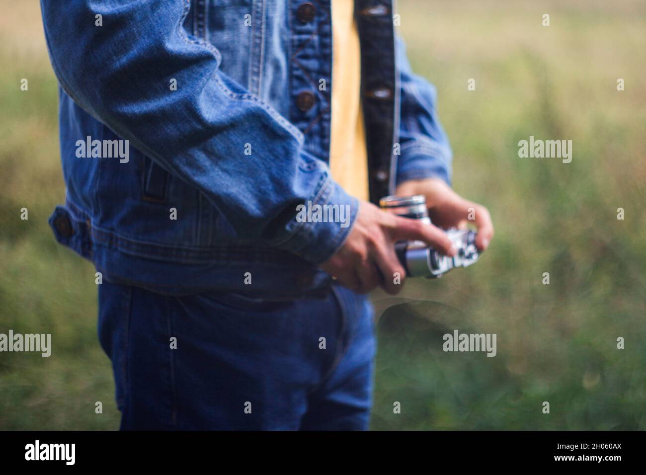 Defocus male hands holding retro photo camera on green nature background. Film grain effect. Man in jeans taking photo, selfie on vintage camera. Out Stock Photo