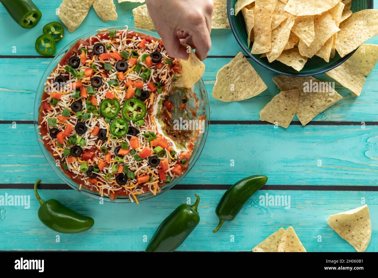 A hand dipping a tortilla chip into a homemade Mexican 7 layer dip