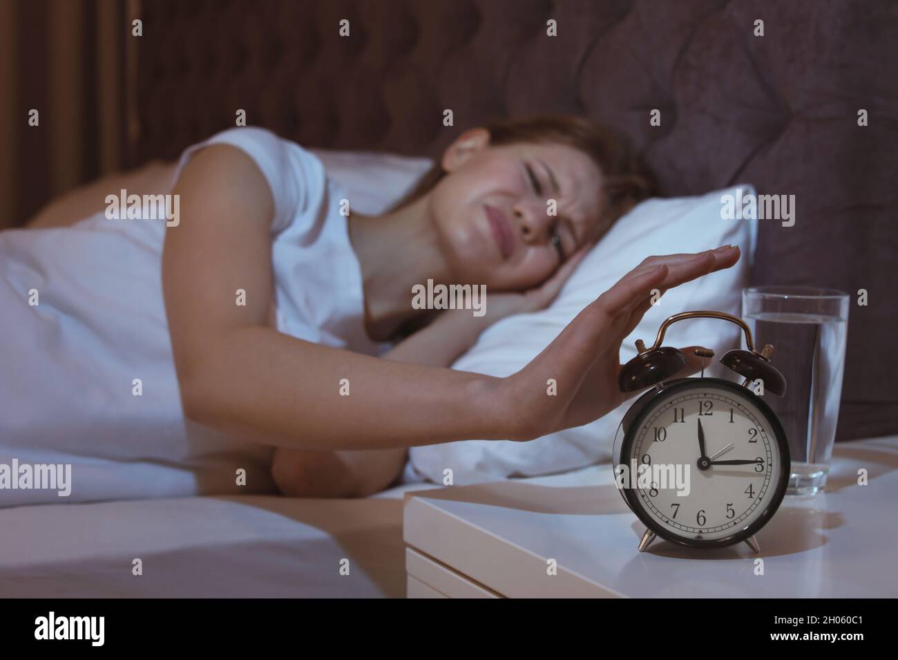 Young woman with terrible headache at night trying to turn off alarm