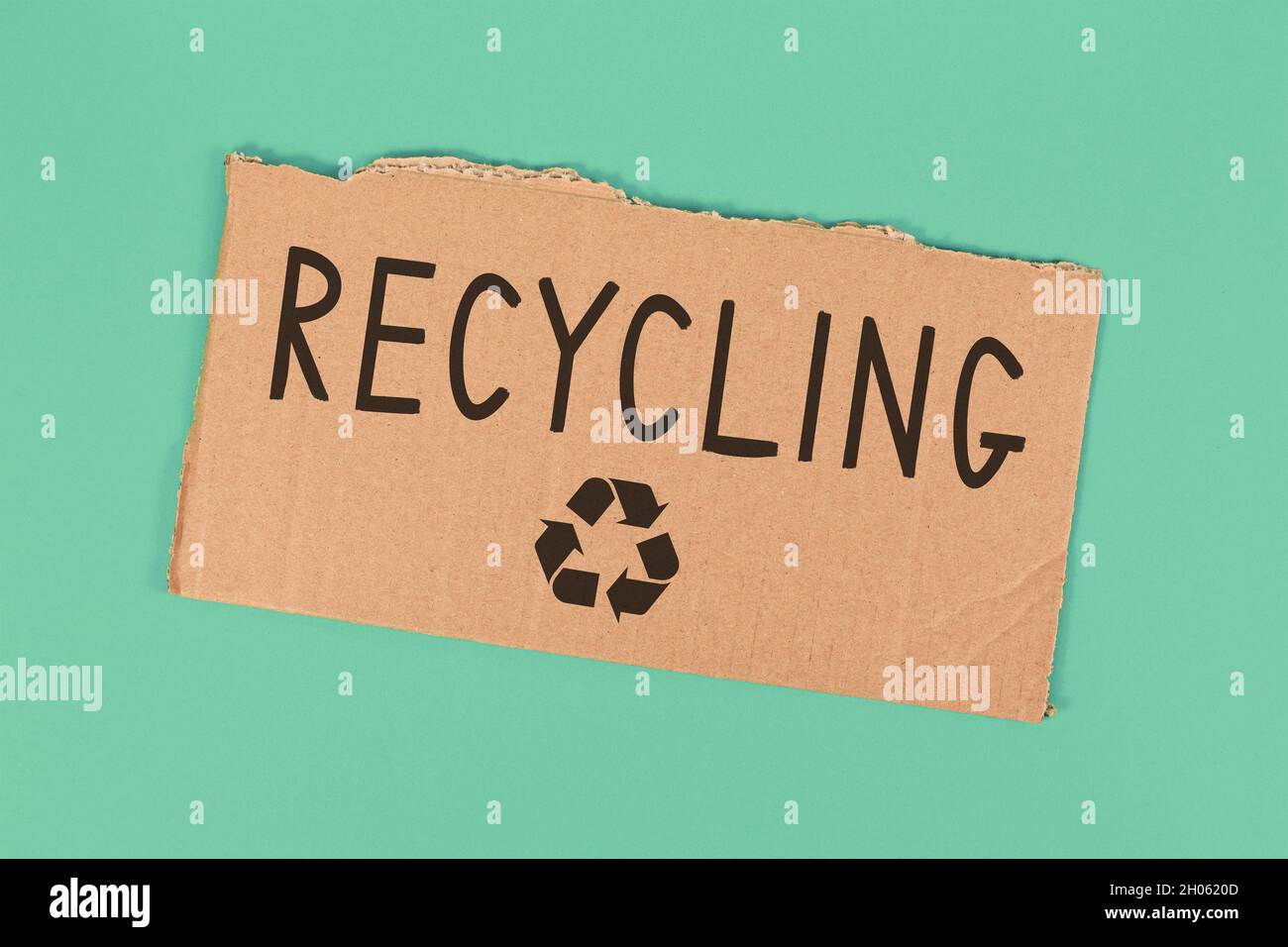 Recycling text and arrow symbol on piece of cardboard on green background Stock Photo