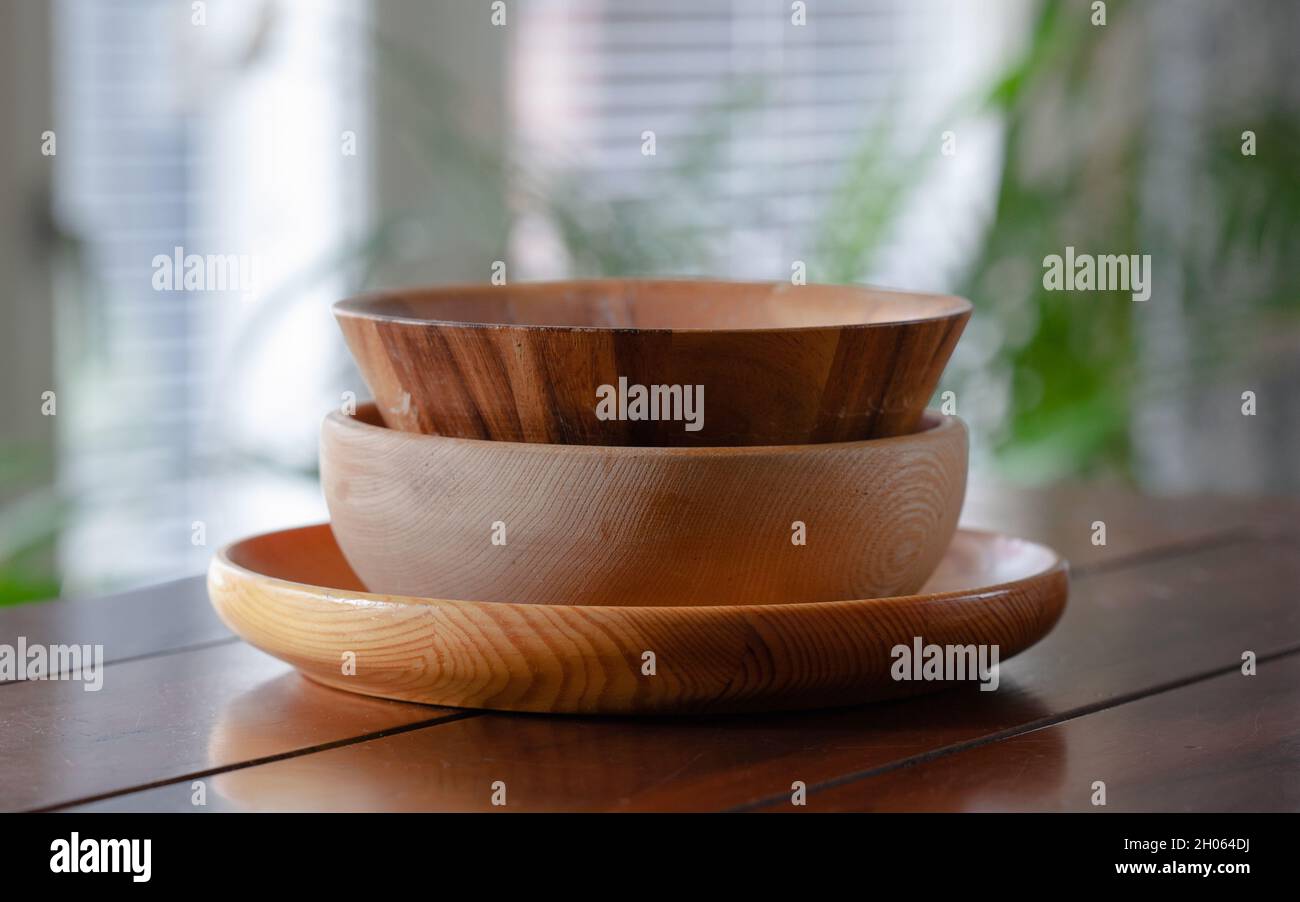 Three different kinds of wooden bowls stacked on wooden table. Stock Photo