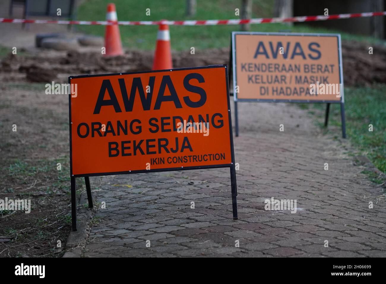 Working on site sign with orange and black text. The written text wrote in Malay means be caution people is working Stock Photo