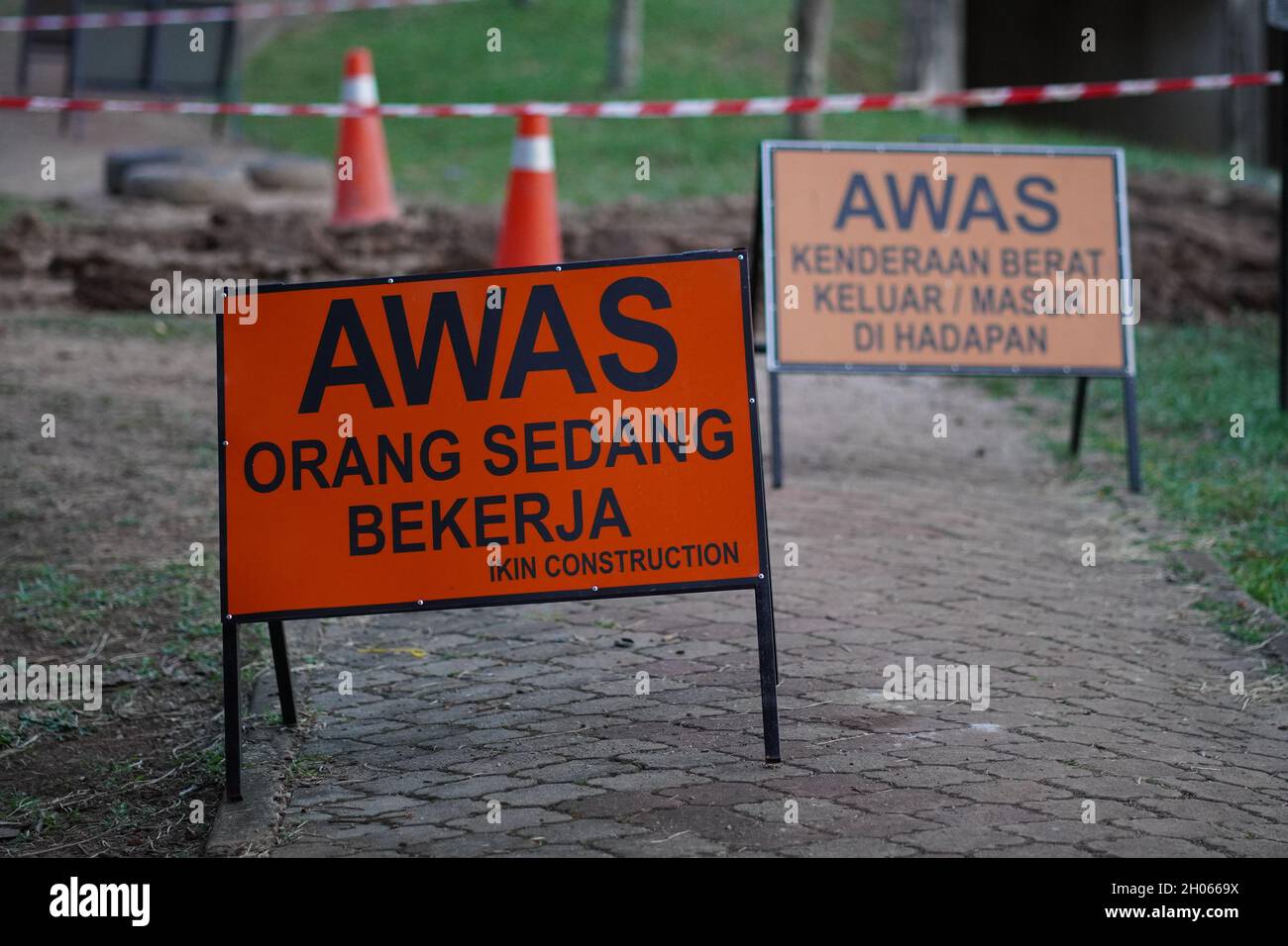 Working on site sign with orange and black text. The written text wrote in Malay means be caution people is working Stock Photo